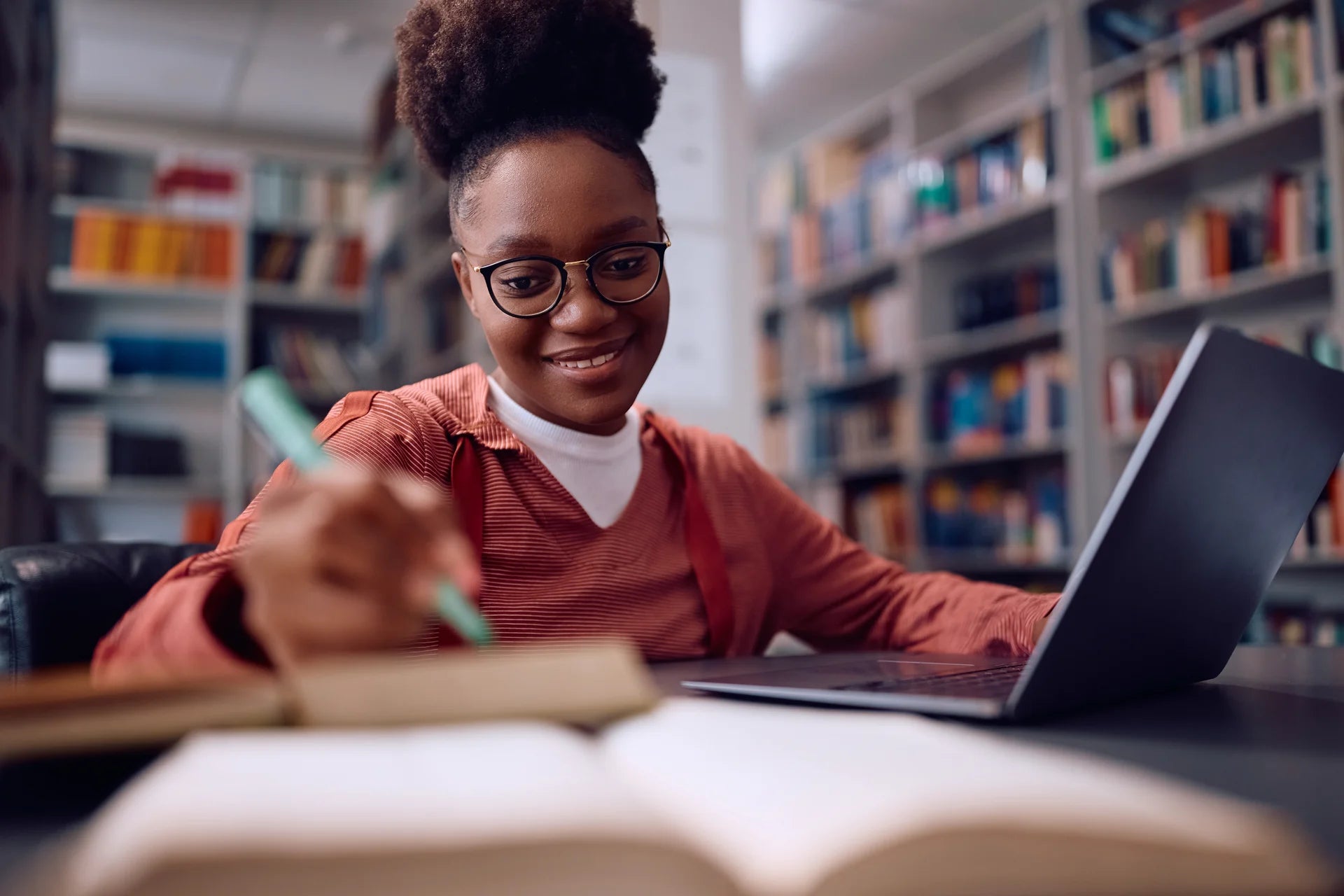 A learner studying with a laptop and notebook in a library